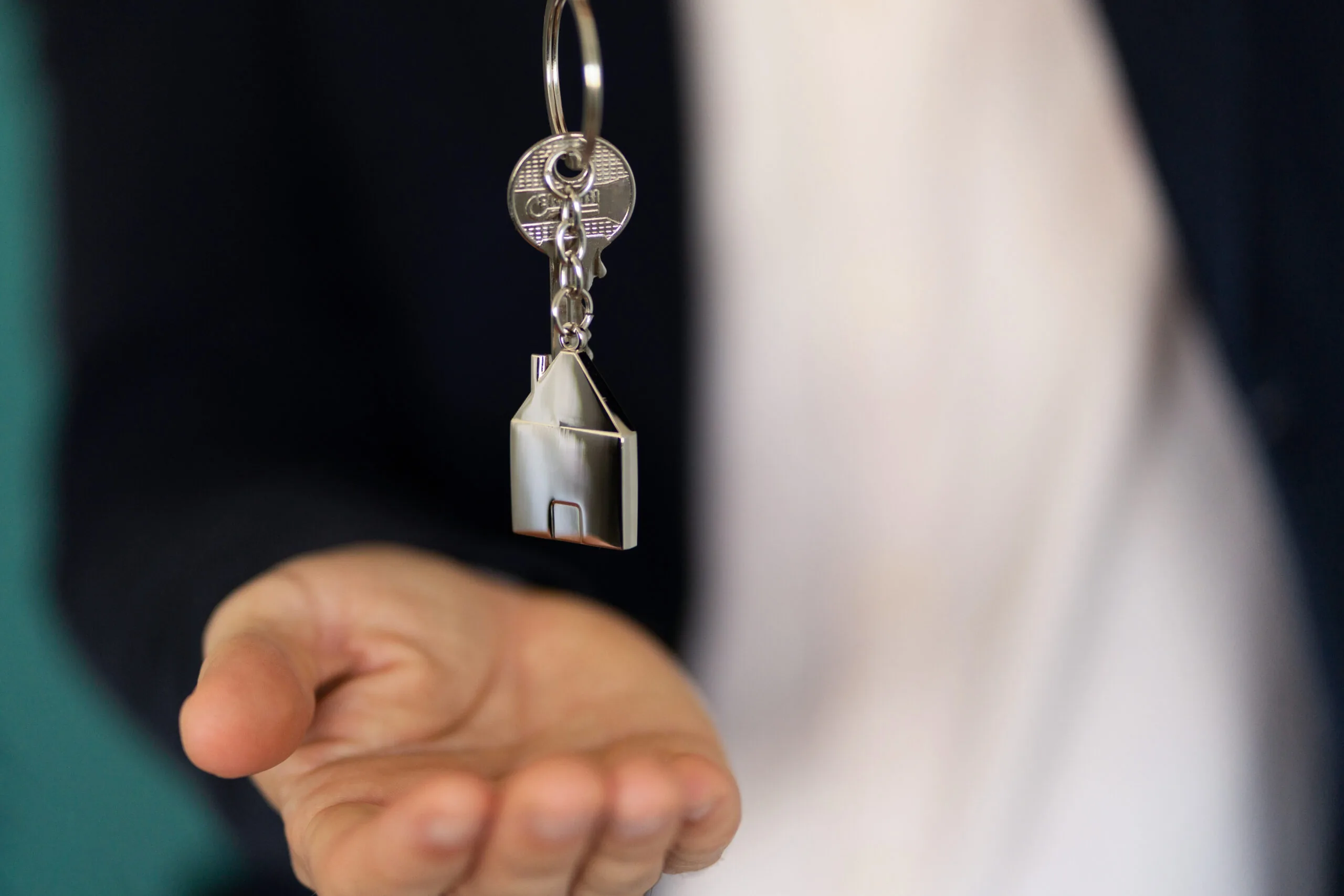 uitgestoken hand met een sleutel aan een huisvormige sleutelhanger