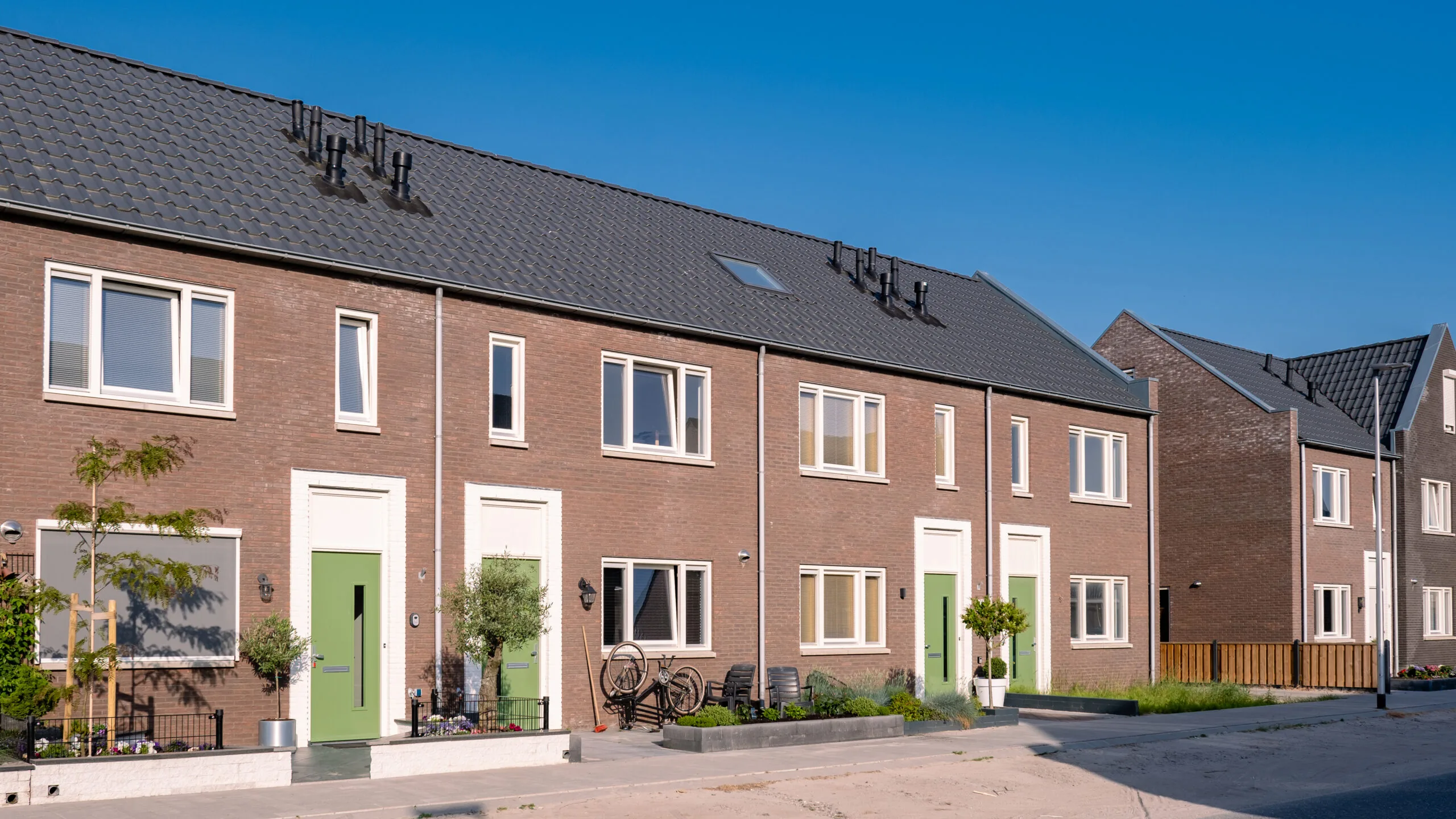 rij moderne bakstenen gezinswoningen met groene voordeuren onder een blauwe hemel