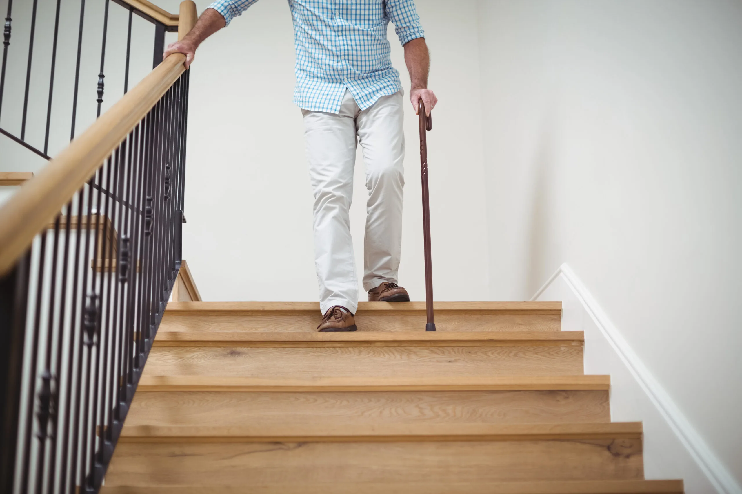 oudere man daalt met wandelstok en hand aan de leuning de trap af